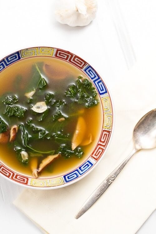 Kale and mushroom soup in bowl with spoon.