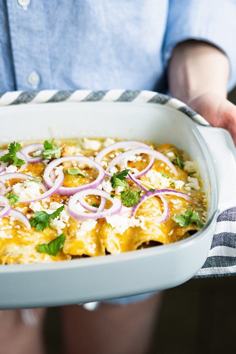 Hands holding enchiladas in pan