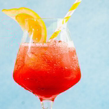 Campari spritz in glass with lemon wedge and straw.