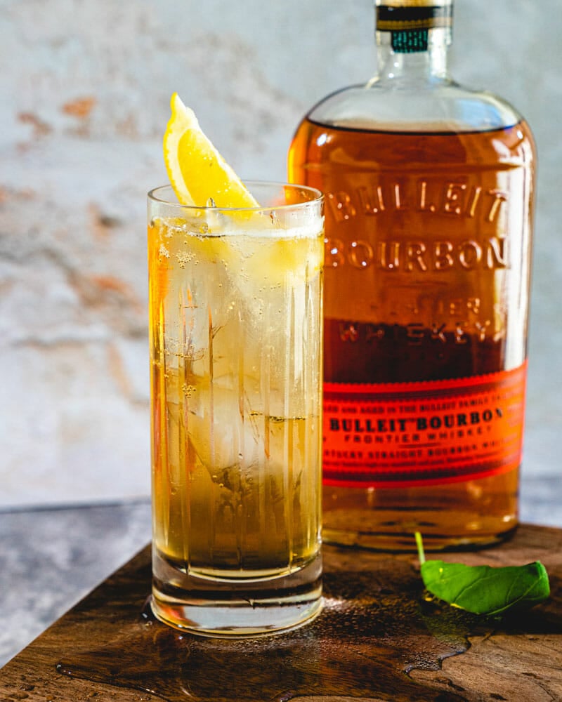 Whiskey highball with lemon slice and bourbon bottle