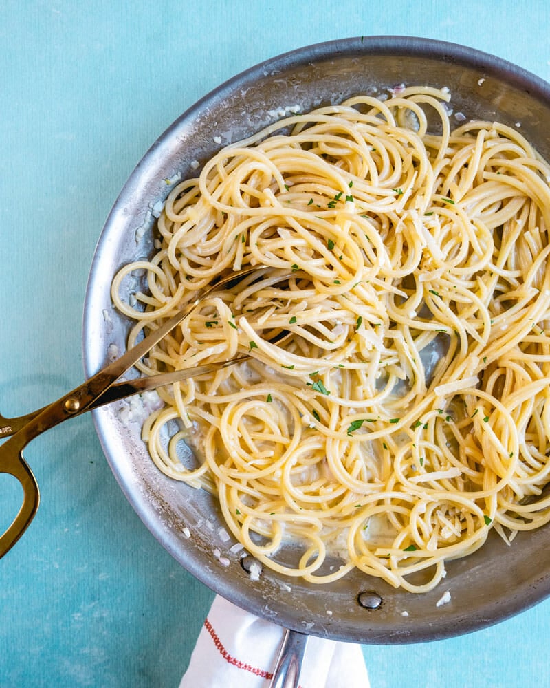 White wine sauce on pasta in pan with tongs