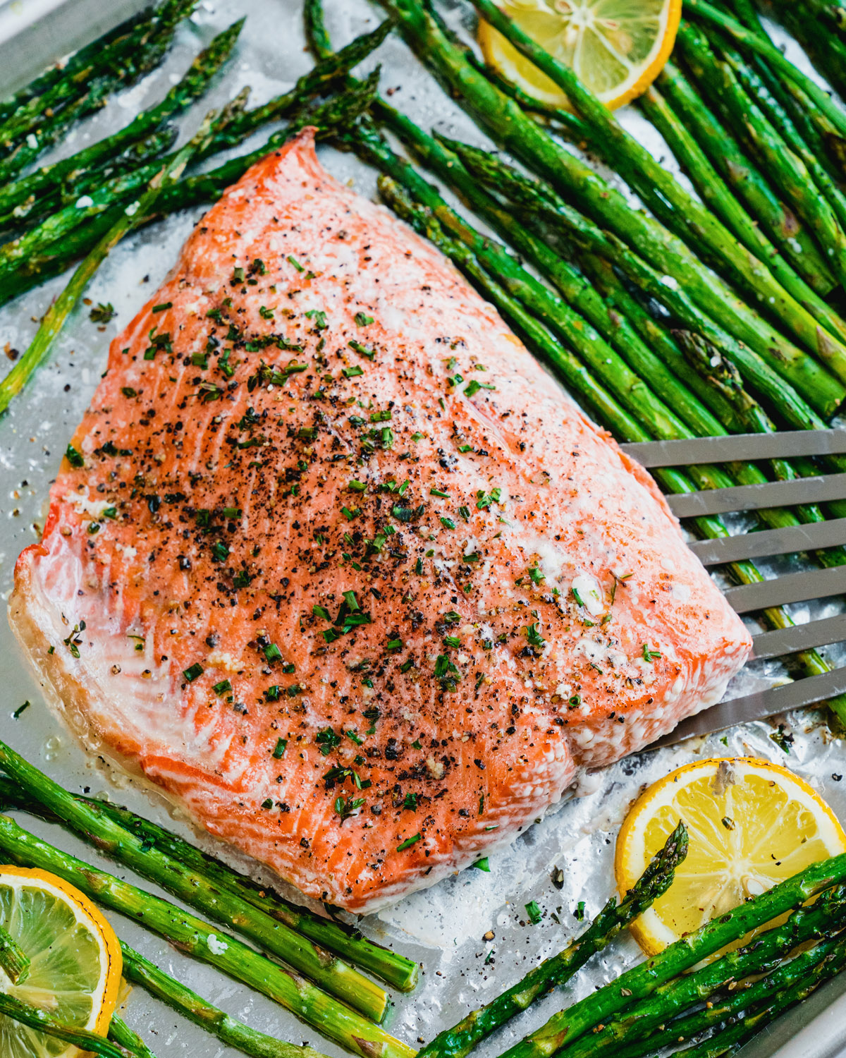 Baked salmon and asparagus on foil lined sheet pan with lemon slices. 