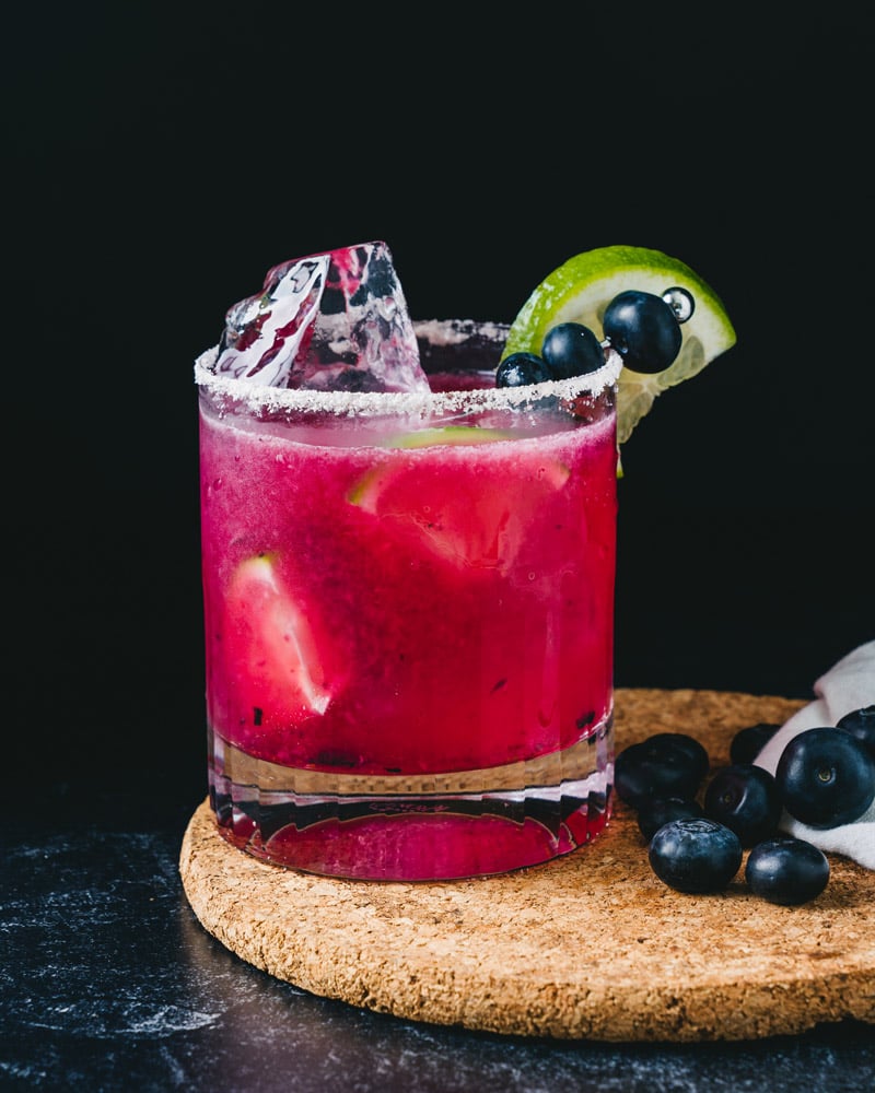 Blueberry margarita in rocks glass with blueberries and lime wedge. 