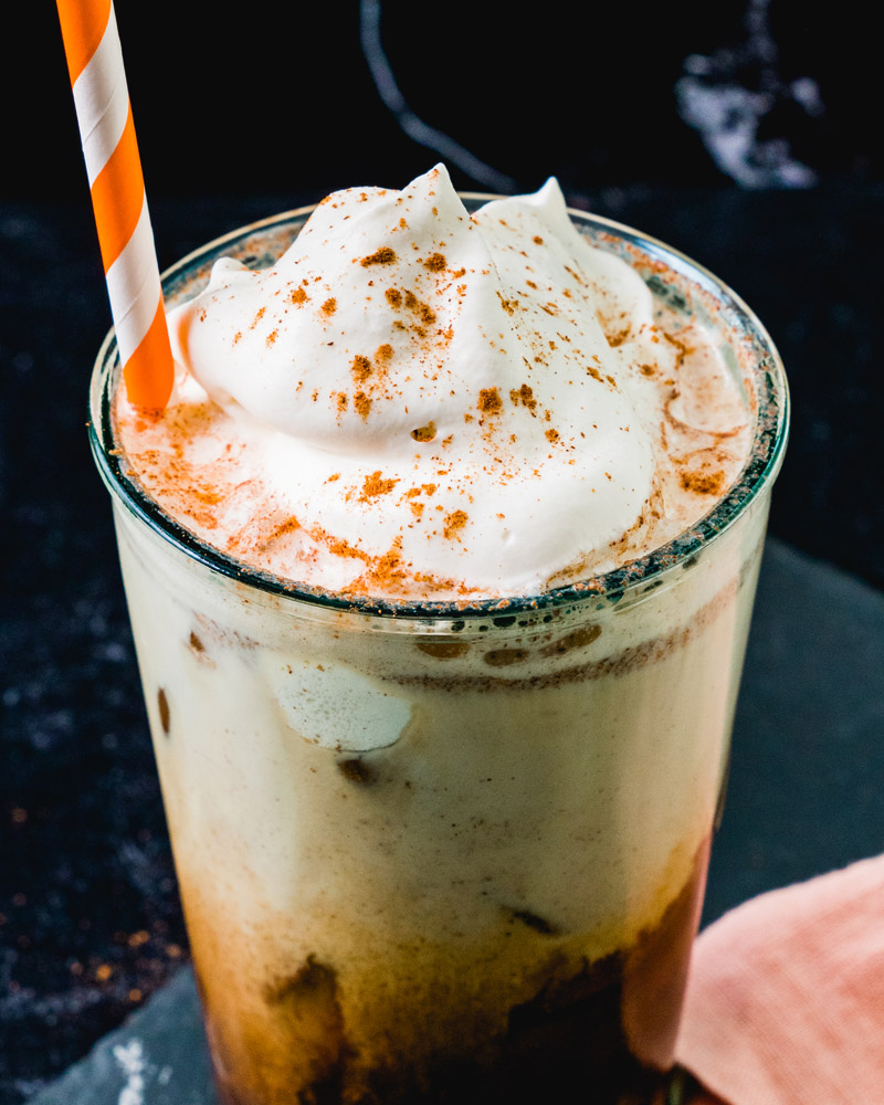 Iced Pumpkin Spice Latte in tall glass with orange straw