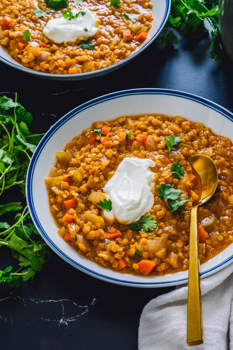Red lentil soup recipe in bowl with spoon and yogurt garnish