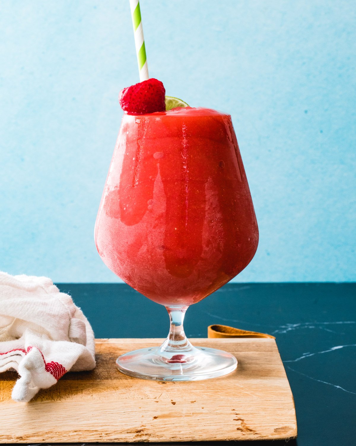Strawberry daiquiri recipe in glass with straw and strawberry garnish.