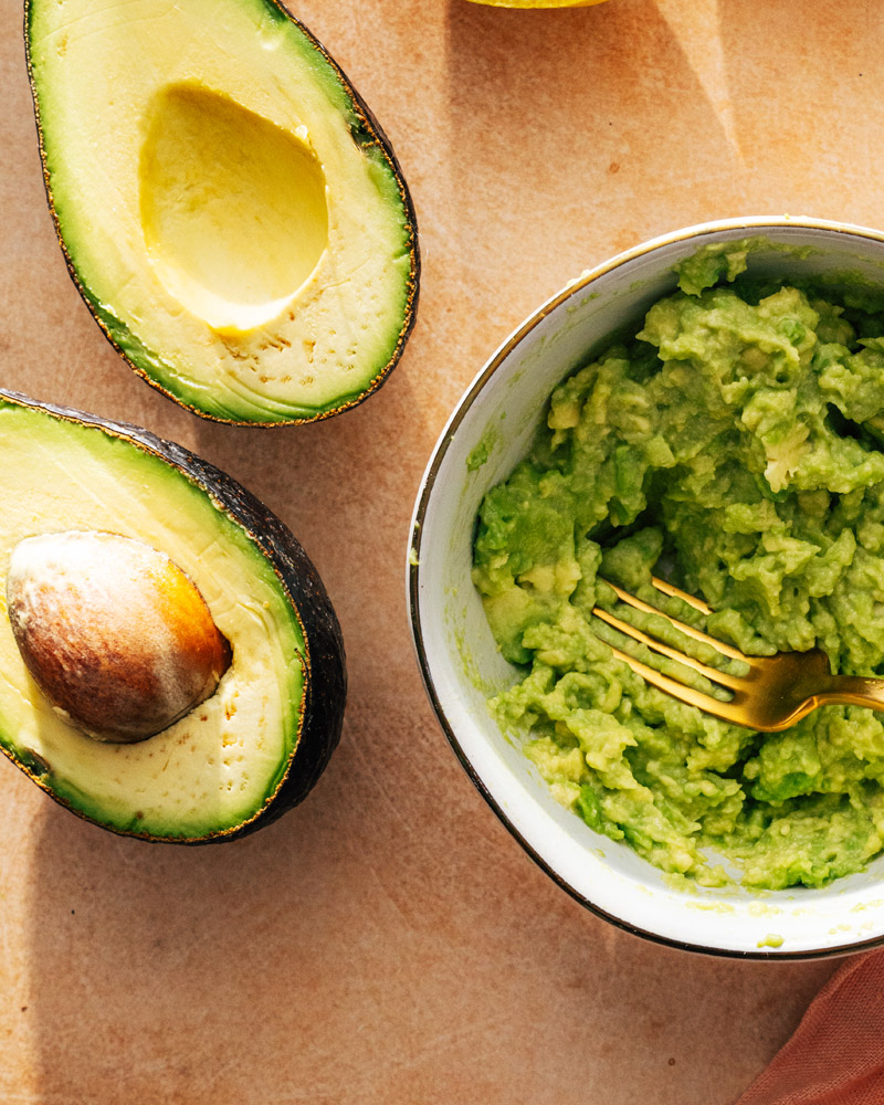 Avocado cut open alongside a bowl of mashed avocado.