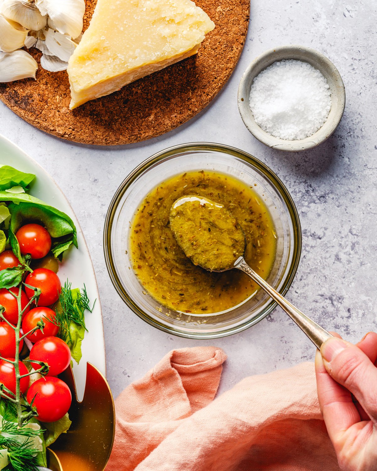 Italian Dressing in bowl with spoon, salad, and Parmesan cheese.