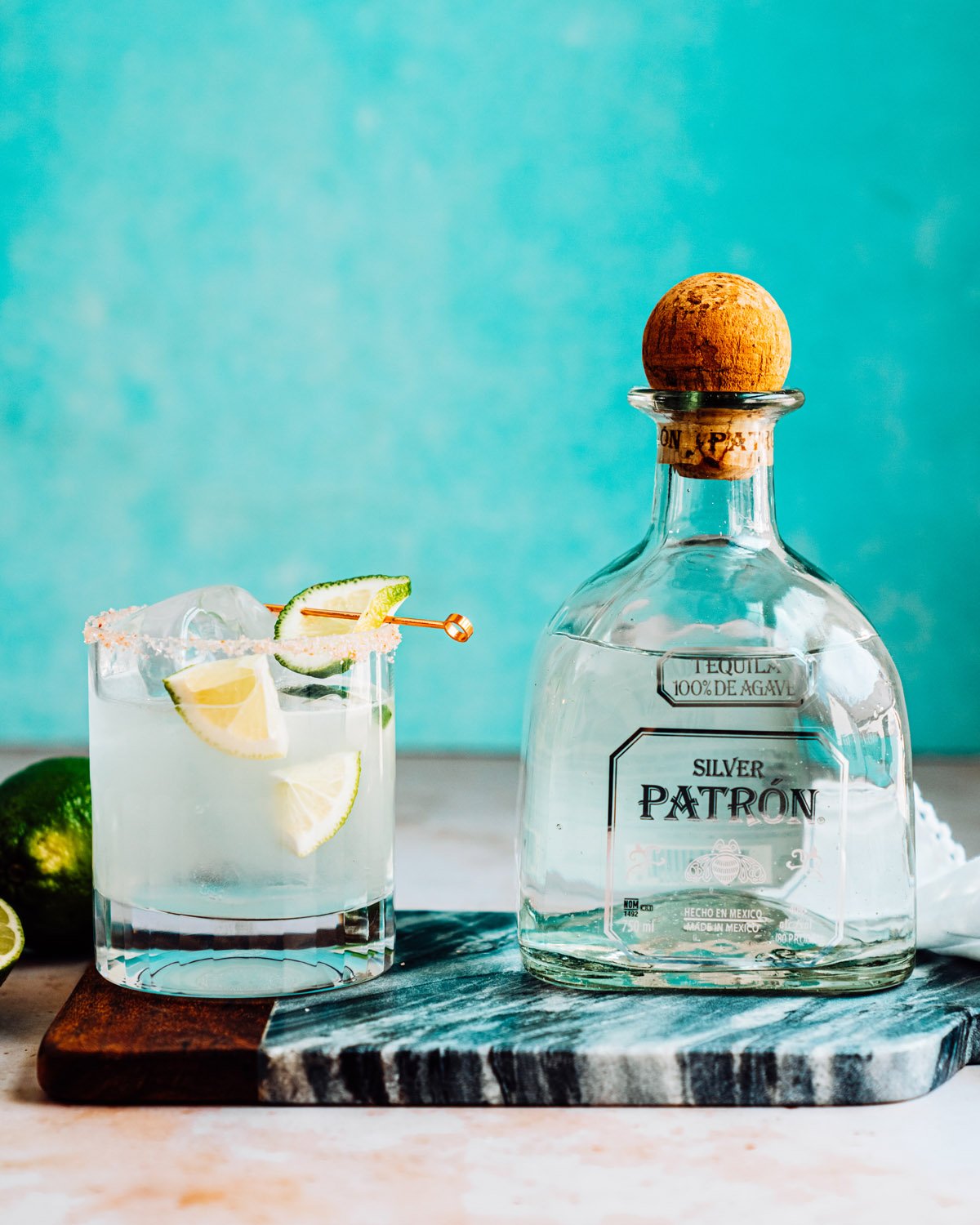 Margarita ingredients: tequila and limes with margarita recipe in glass.