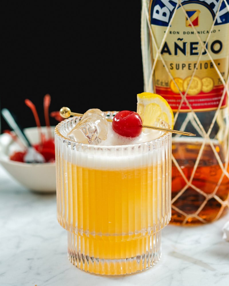 Rum sour cocktail with dark rum bottle.