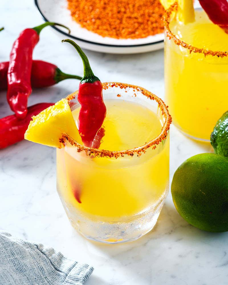 Spicy Pineapple Margarita  in a glass with Tajin rim and spicy pepper garnish