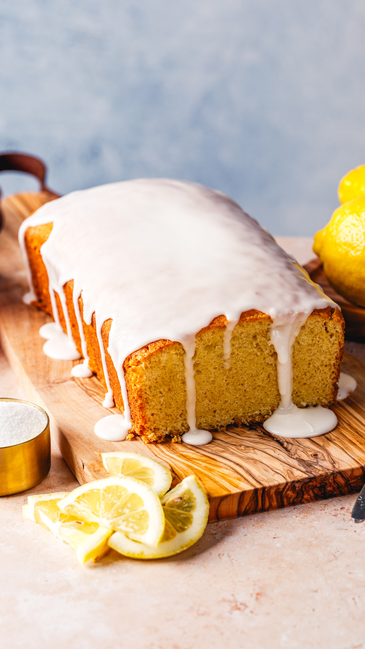 Lemon Bread recipe with lemon icing drizzle on cutting board with lemon slices. 