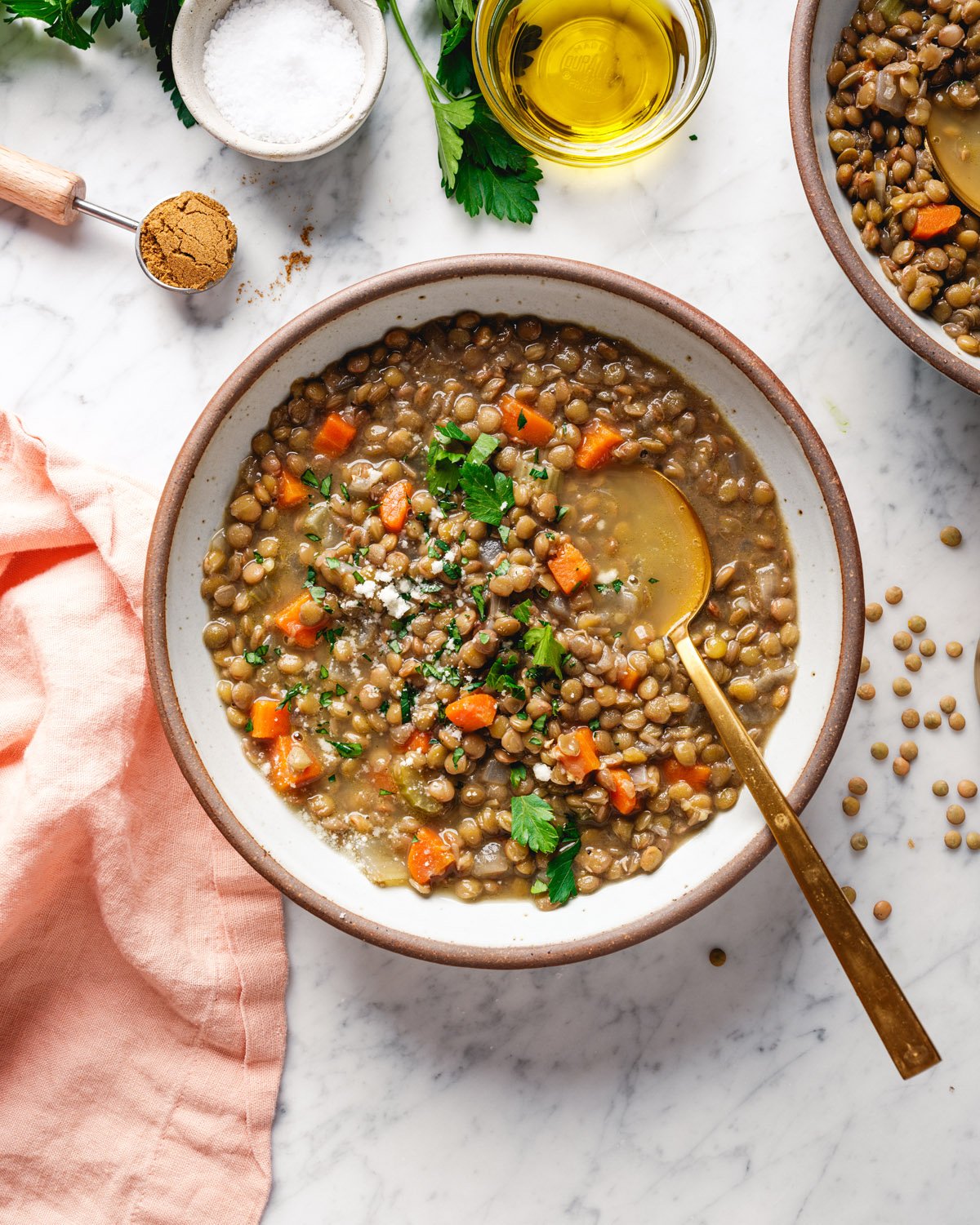 Lentil soup in bowl with cumin, olive oil, salt and lentils in background.