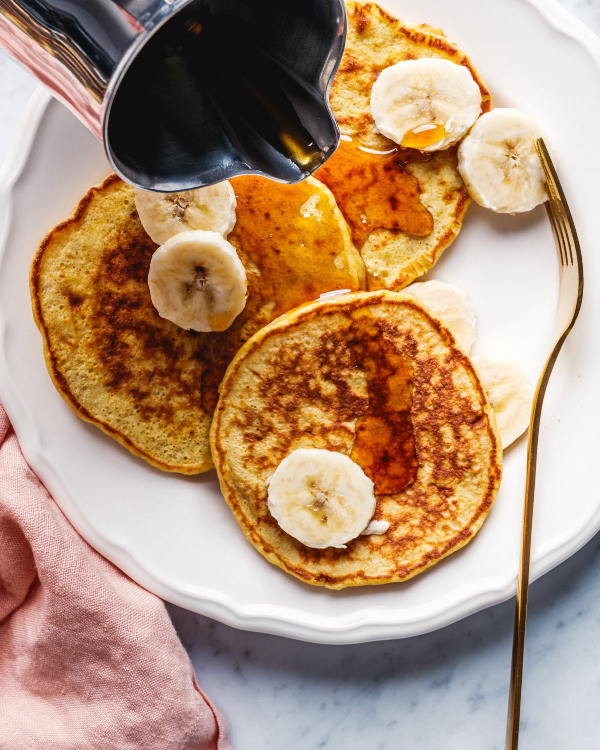 Banana pancakes with sliced bananas and syrup pouring.