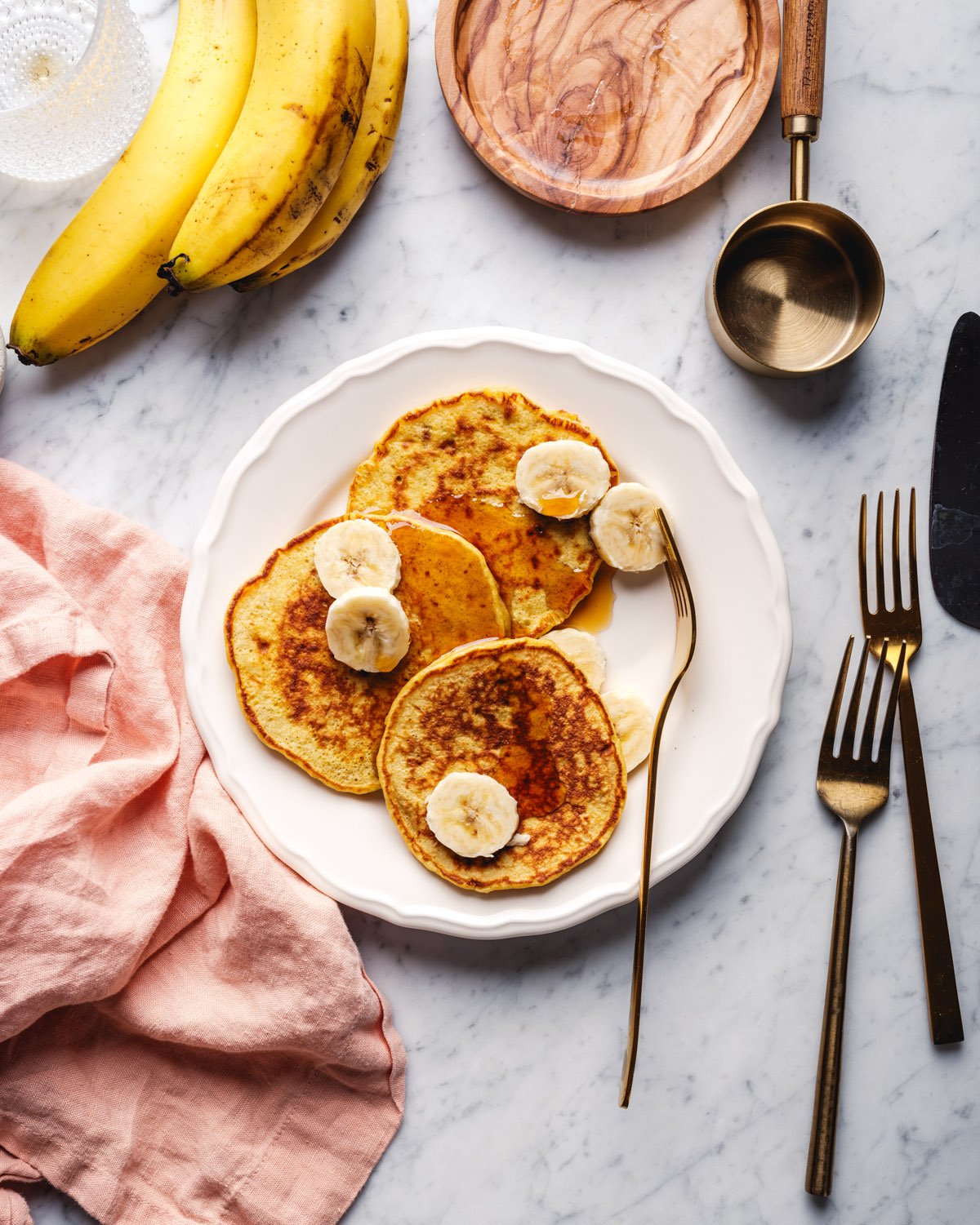 3 ingredient banana pancakes with bunch of bananas, breakfast set up, and napkins.