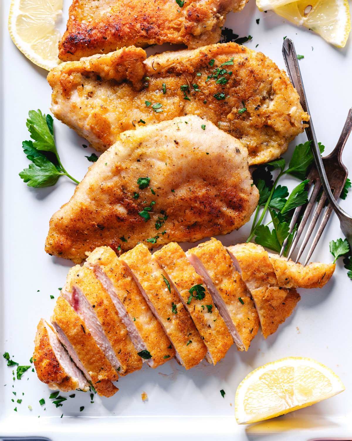 Parmesan Crusted Chicken sliced on a platter with parsley and lemon. 