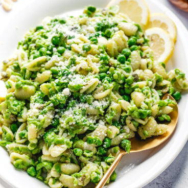 Pasta with Peas on a plate with serving spoon and lemon slices.