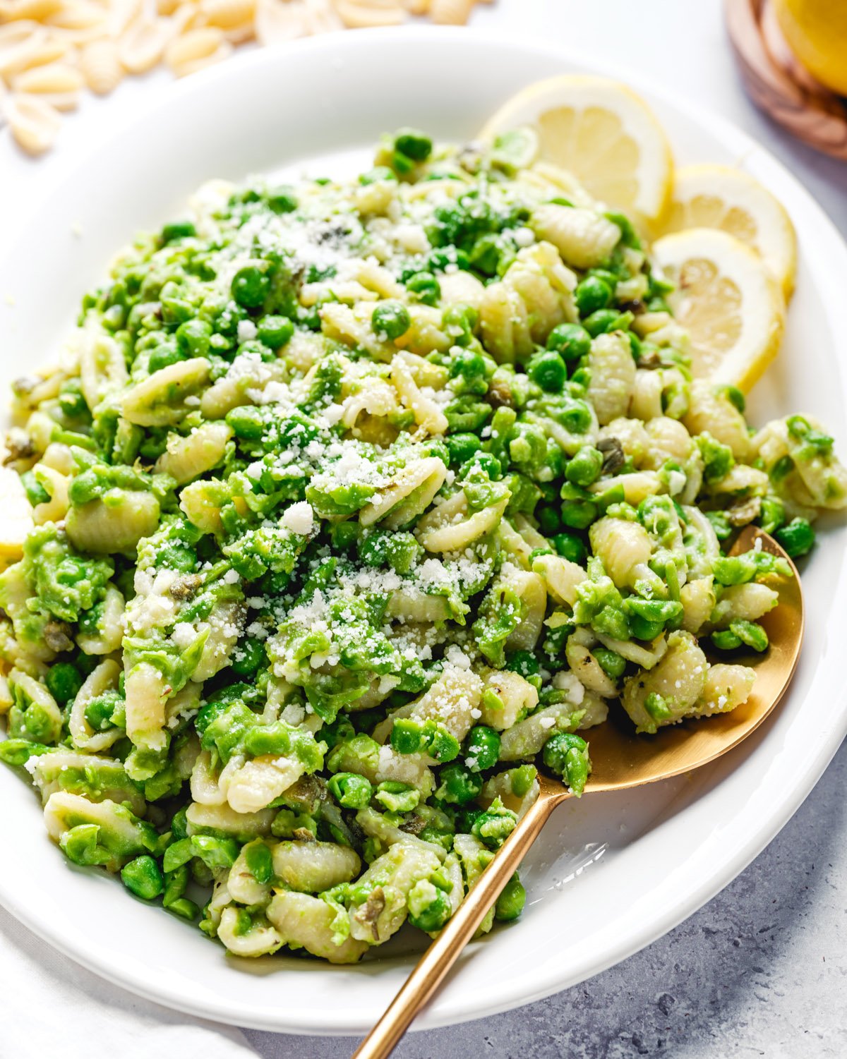 Pasta with Peas on a plate with serving spoon and lemon slices.