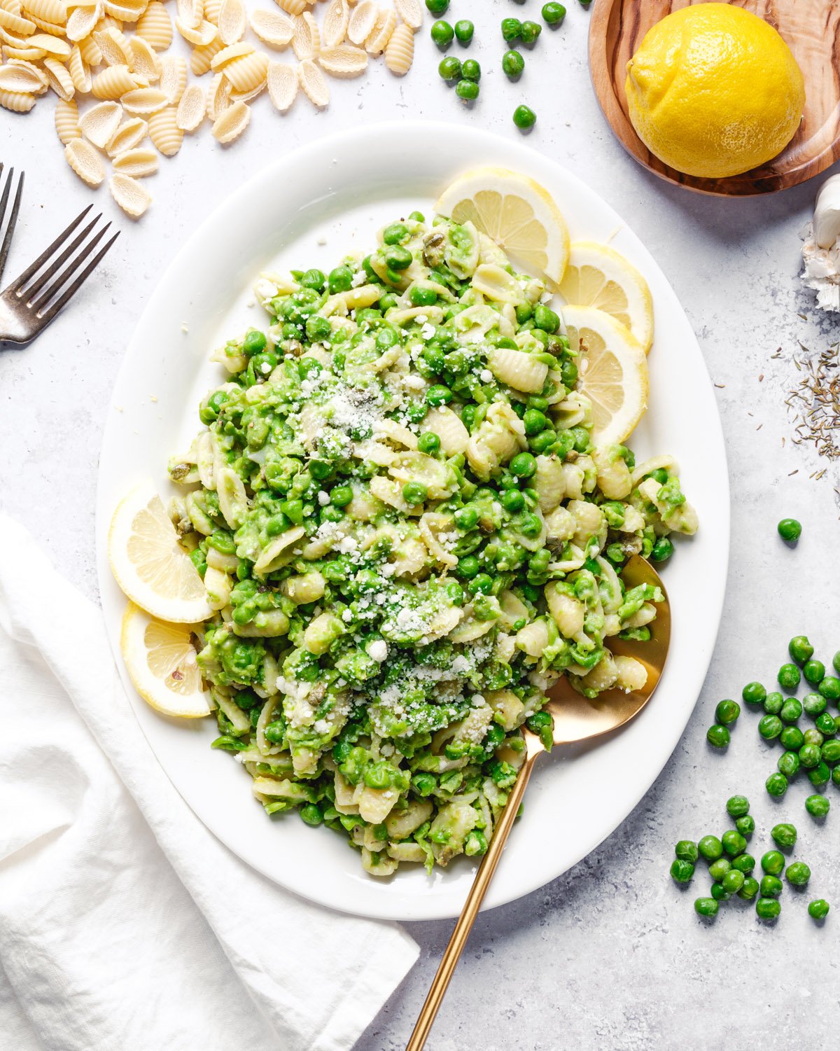 Pasta with peas on plate with serving spoon, peas, and lemons.