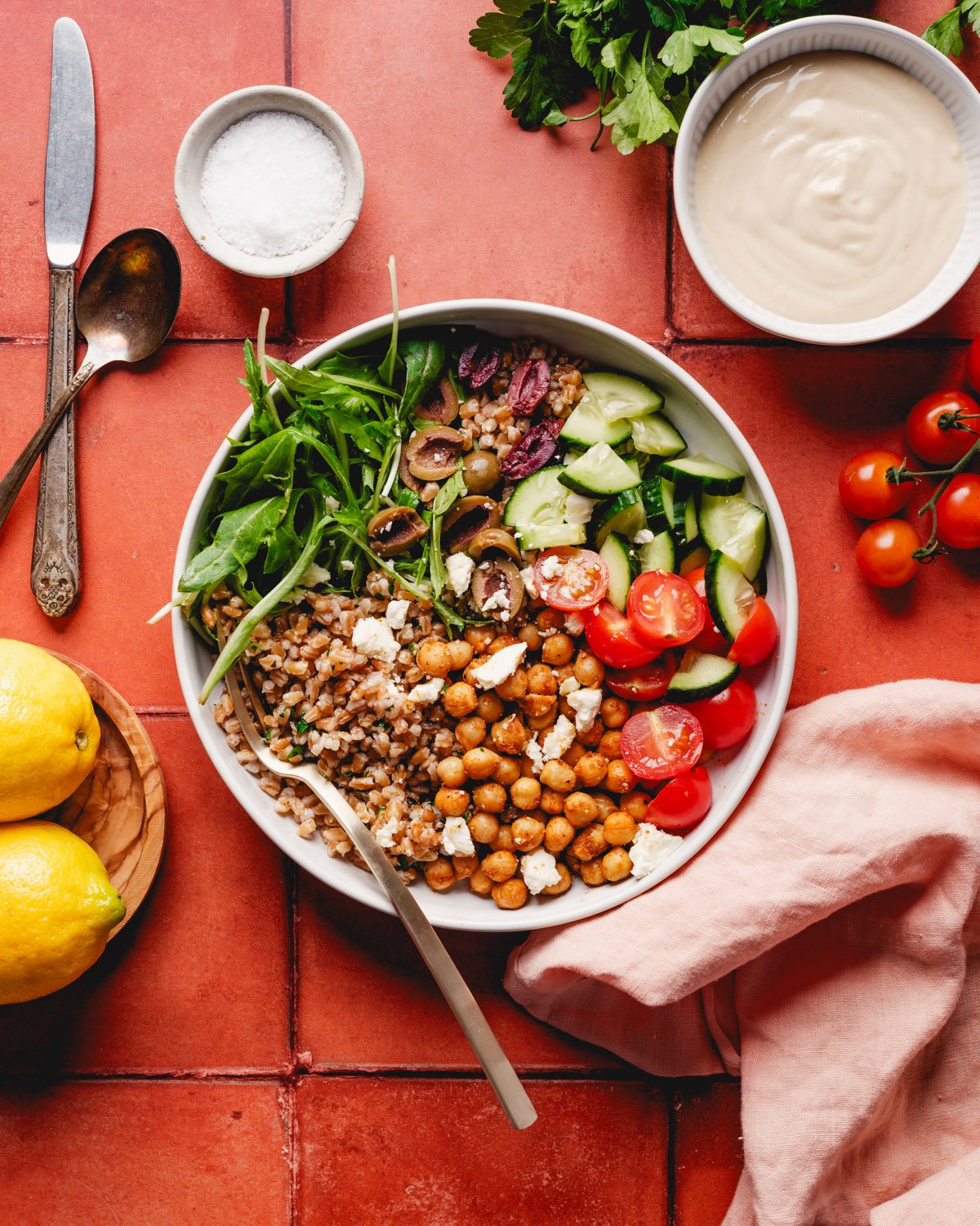 Farro bowl recipe in bowl with tomatoes, hummus dressing, and lemons around
